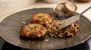 Shami Kabab Parath Roll taway par shallow fry ho rahe hain, ek spatula se unhe mash kiya ja raha hai.